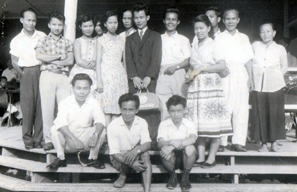 Simon, wearing a black suit, being sent off by his family to New Zealand in 1959 at the old Jesselton Airport. His mother is first from the right and his father is second from the right (standing). His youngest brother, Stephen, is seated first from the right. 