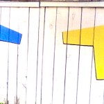 Two T-shirts painted on a fence: one yellow (right), the other blue